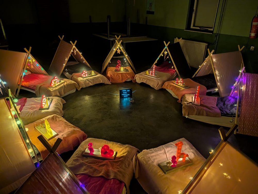 Een grote kring tipi&rsquo;s met lichtjes in een verduisterde zaal
