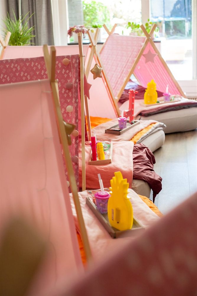 Rij roze tipi&rsquo;s met dienbladen, bekers en lampjes bij het raam